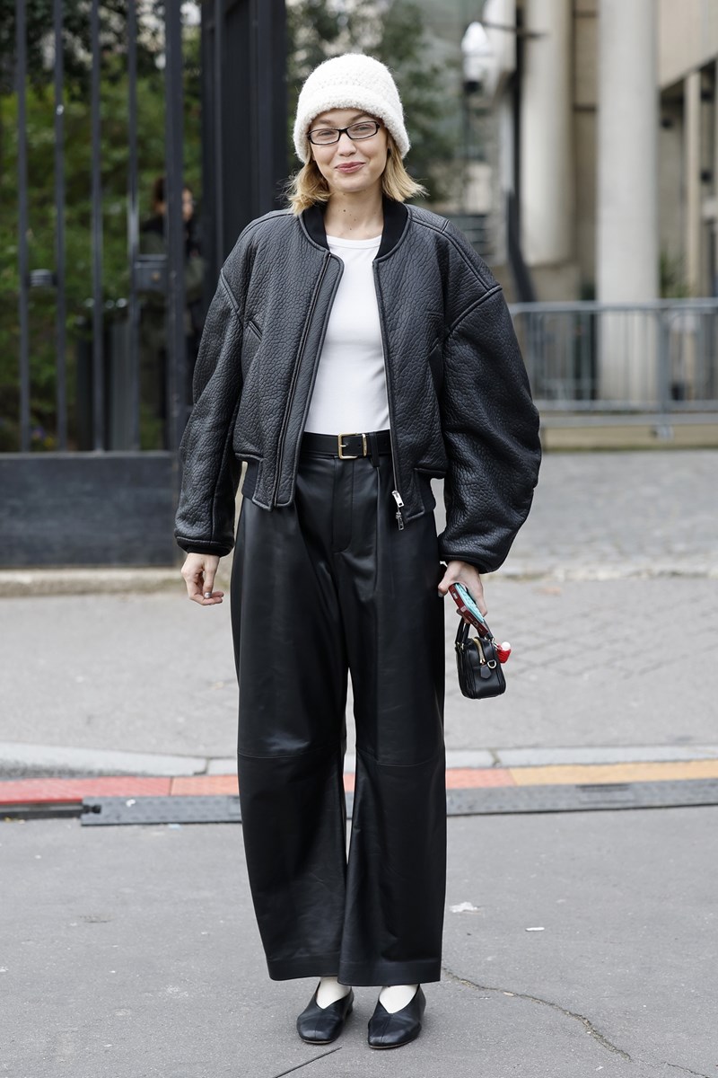 Gigi Hadid wears white top, black leather jacket, black leather pants, black ballet shoes, white beanie, black Miu Miu bag, outside Miu Miu on March 11, 2025 in Paris, France.
